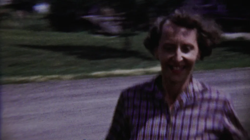 Young runner approaches the handheld camera in a 1958 Saint Francis, Kansas, residential yard scene.
