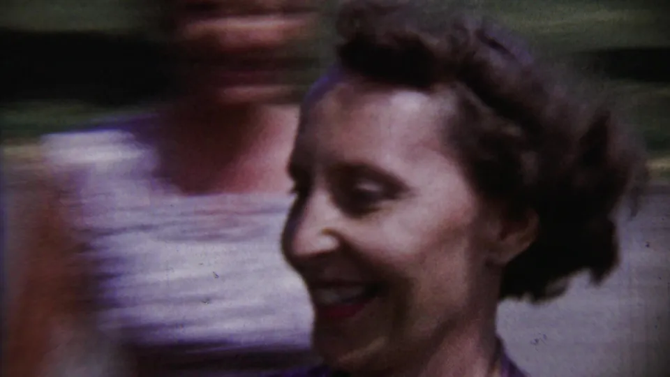 A smiling female face passes close to the camera in blurred 1958 Saint Francis, Kansas home-movie footage, with another person partly visible behind.