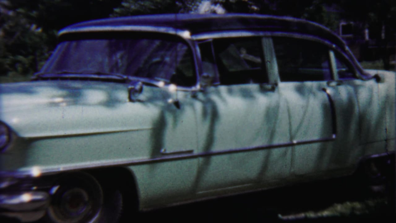 A side view of the pale green sedan shows its long body, dark roofline, chrome side trim, and leafy outdoor surroundings in 1958 Kansas footage.