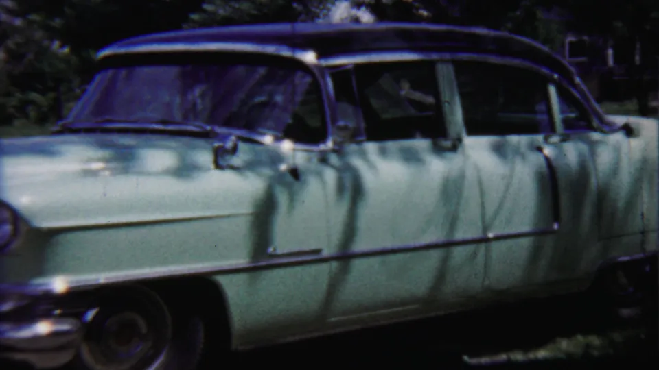 A side view of the pale green sedan shows its long body, dark roofline, chrome side trim, and leafy outdoor surroundings in 1958 Kansas footage.
