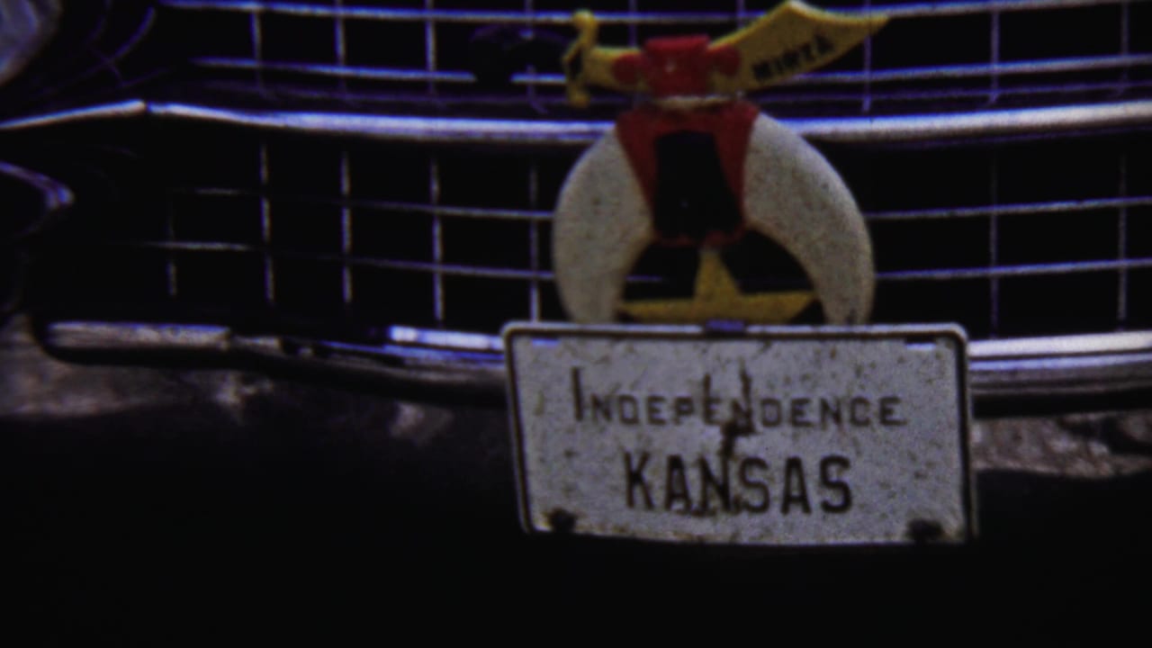 Final close 1958 Kansas frame holding on the classic car grille, ornament, and weathered Independence Kansas plate in grainy 8mm color.
