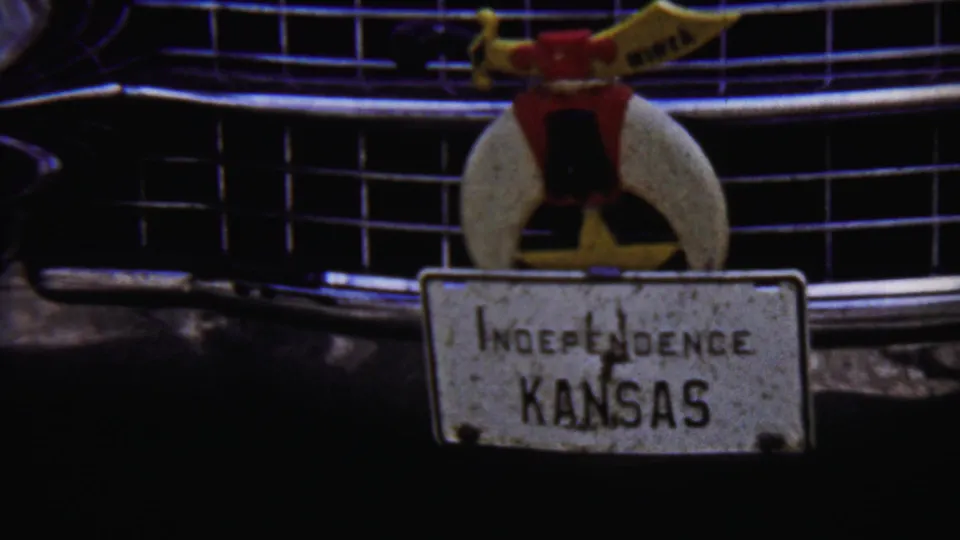 Final close 1958 Kansas frame holding on the classic car grille, ornament, and weathered Independence Kansas plate in grainy 8mm color.
