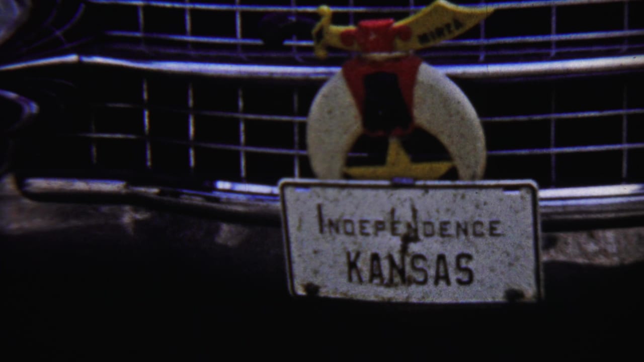 1958 Kansas home-movie frame showing an Independence, Kansas plate mounted on a car front, with a decorative topper above it.