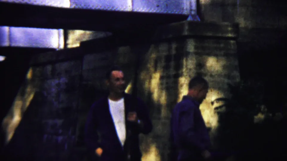 The two men continue through the shaded bridge area in Saint Francis, Kansas, with one carrying a long gun-like object over his shoulder.