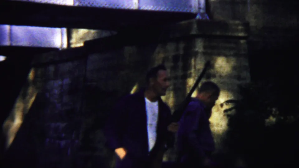 A closer 1958 frame shows the two adult men under the stone bridge, with the long gun-like object held upright near the center.