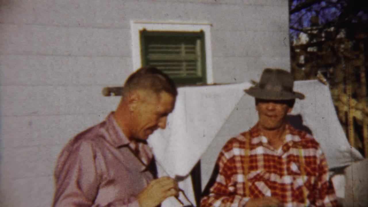 The final 1958 Kansas frame shows one man looking down and another in a plaid shirt and hat standing beside a clothesline outdoors.