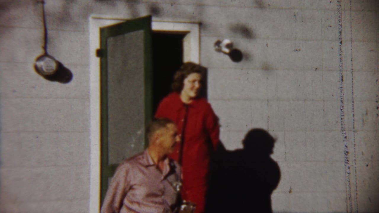 1958 Saint Francis, Kansas home-movie still of a woman in red beside a doorway and a man with a camera in the foreground.