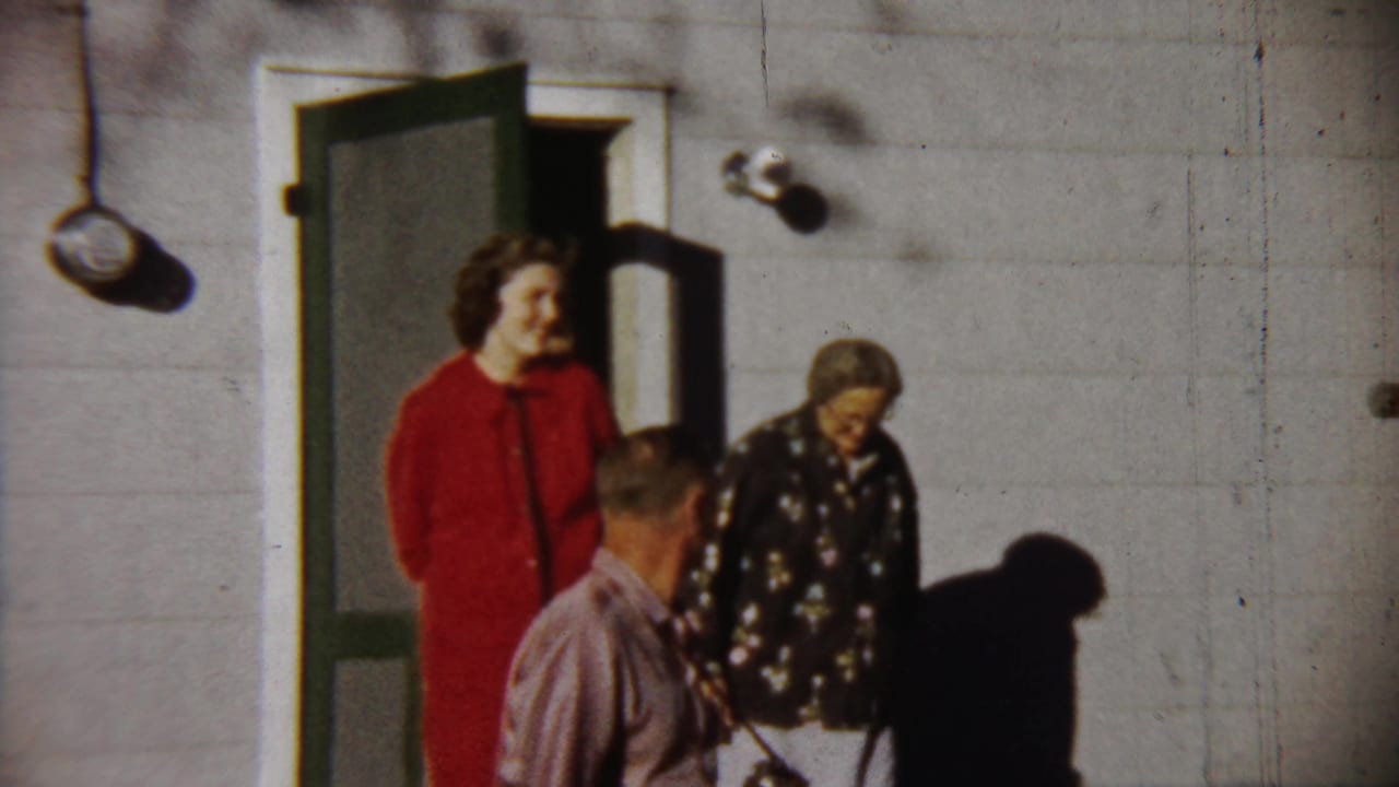 1958 Saint Francis, Kansas frame with a woman in red, another woman in patterned clothing, and a man gathered outside a house.