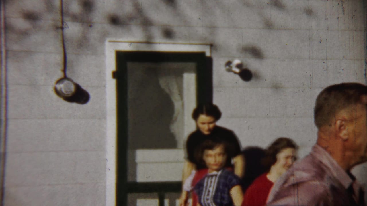 Saint Francis, Kansas home-movie frame with people gathered by a house entrance and a man moving out of frame.