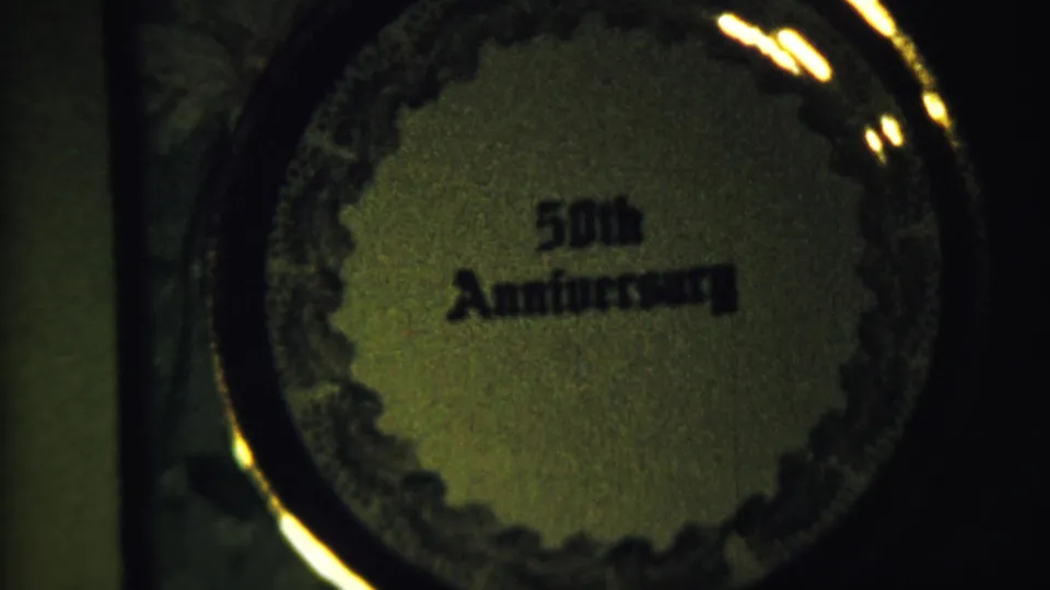 Close 8mm view of a circular 50th Anniversary plaque with decorative edging and warm reflections.