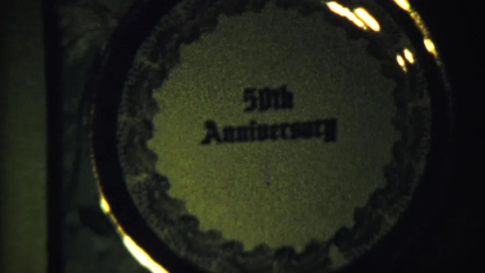 Close 1958 8mm frame of the 50th Anniversary plaque, softly lit against a dark background.