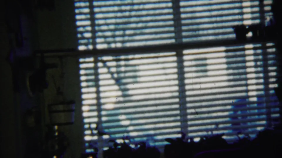 1958 Saint Francis, Kansas 8mm frame of an interior window with horizontal blinds and bright daylight beyond.