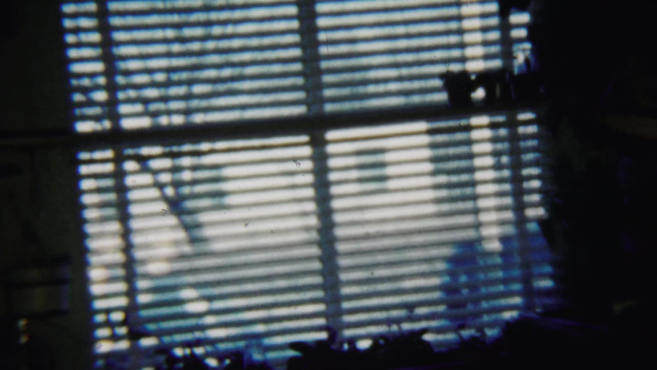 Dim room with horizontal window blinds casting striped light and shadow.
