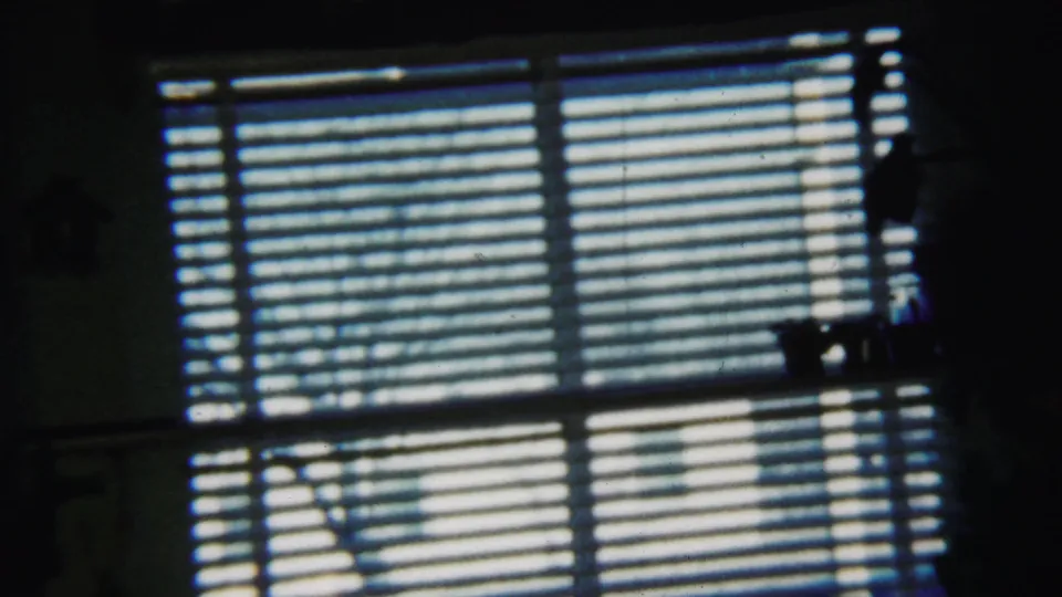 1958 home interior frame from Saint Francis, Kansas, showing horizontal blinds, bright exterior light, and shadowed room details.