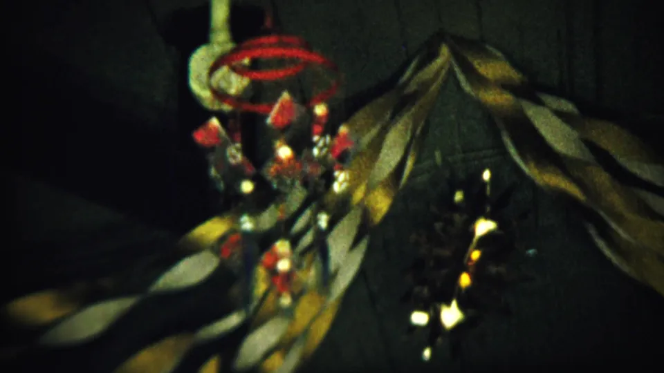 Grainy 1958 home-movie frame showing a red and white suspended decoration in a dim Saint Francis, Kansas room.