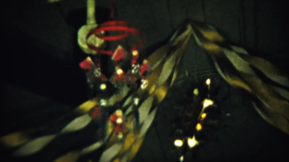 Final 8mm frame of the dim interior ornament, with red accents and warm reflections near a draped surface.
