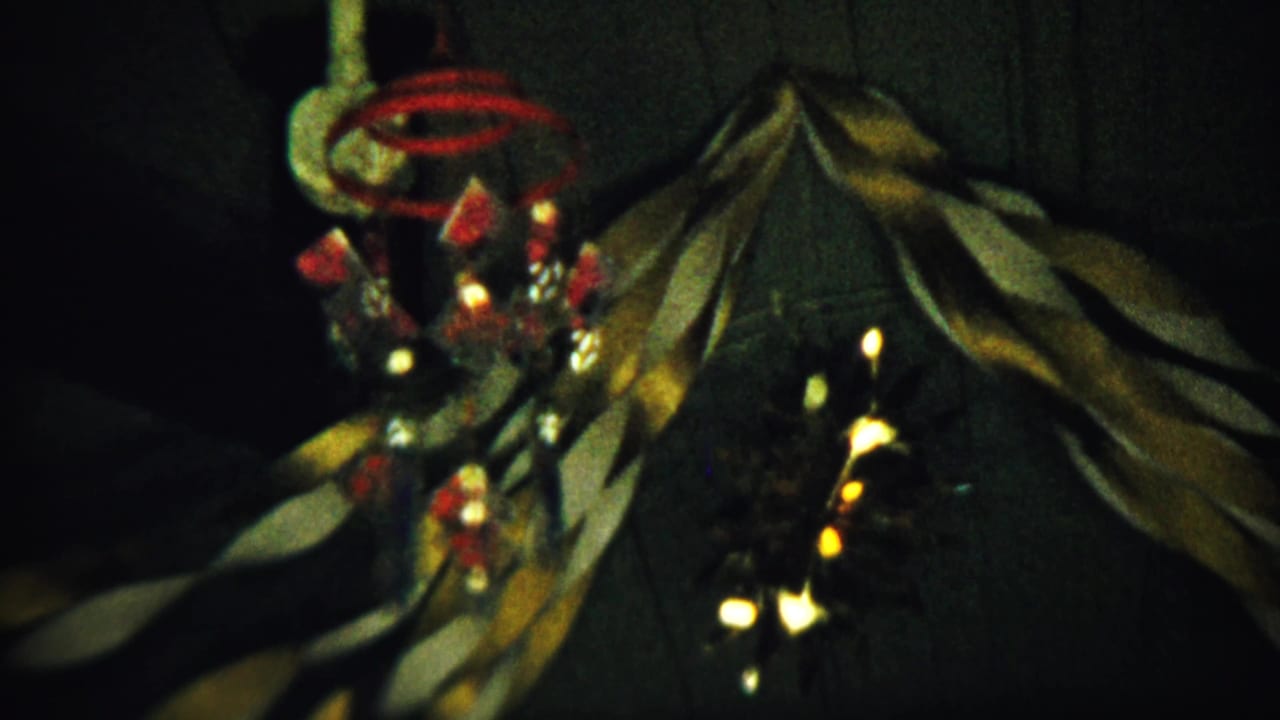 Christmas garland, red ornaments, and glowing string lights hang against a dark wall.