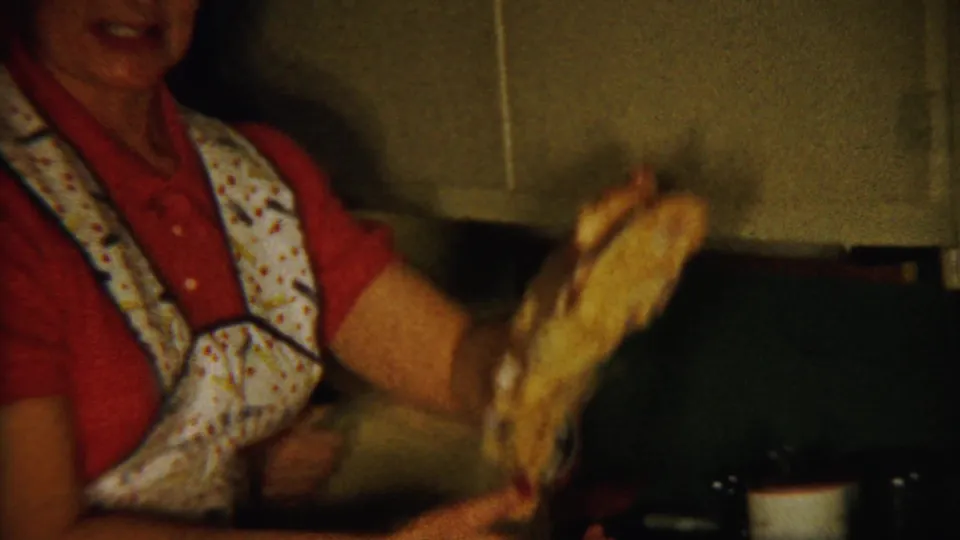 A woman in a red shirt and patterned apron lifts a pale piece of food or dish in the Saint Francis kitchen interior.
