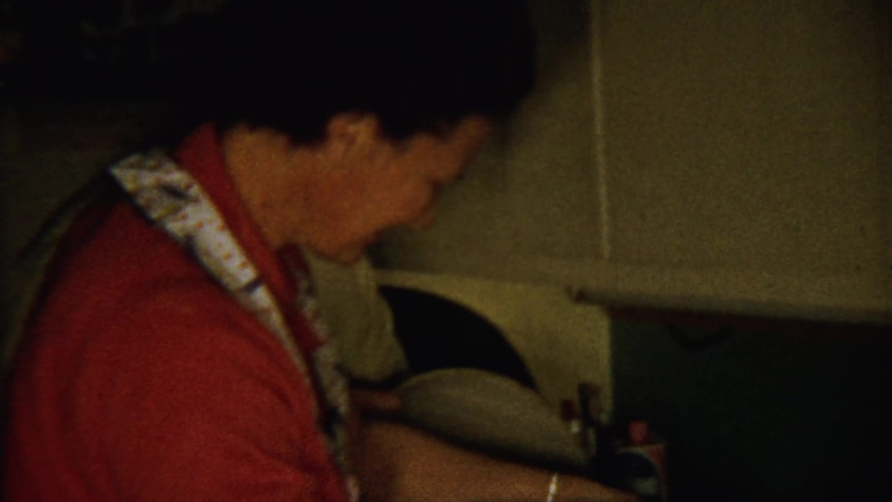 Woman in profile leaning over a kitchen counter in low light.