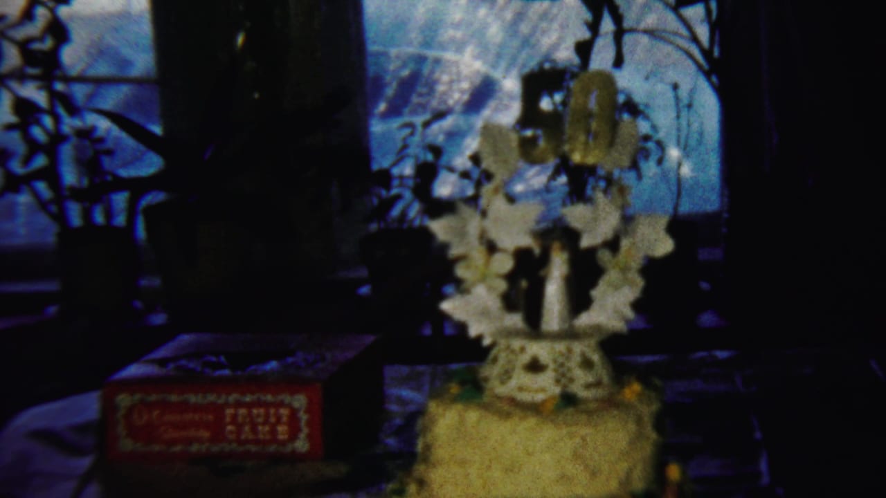 Decorated tiered cake and red fruit cake box in dim window light.