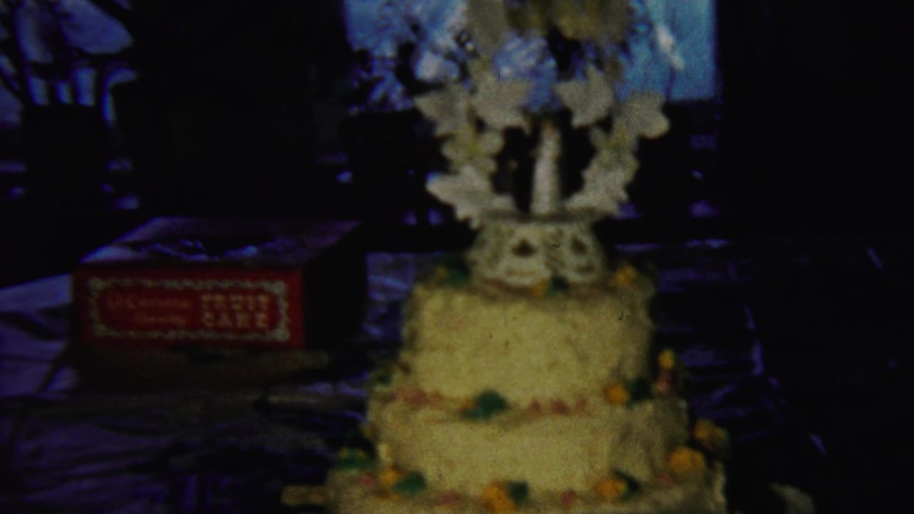 Three-tier yellow cake on a dark table beside a red fruit-cake box.
