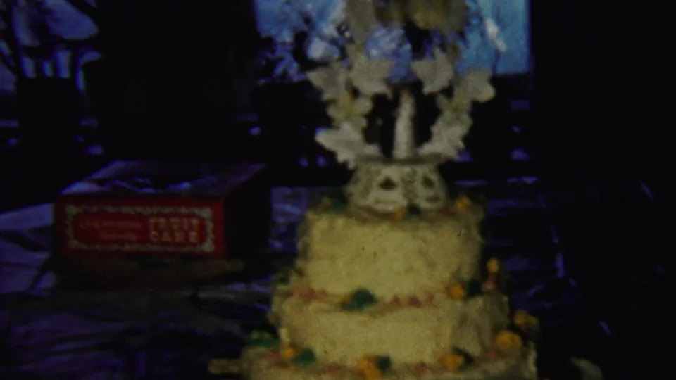 1958 Saint Francis, Kansas home-movie frame showing a decorated three-tier yellow cake with a red fruit-cake box nearby.