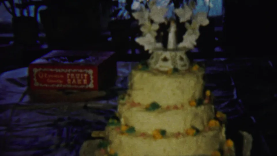 Closer 8mm view of the yellow tiered celebration cake and red fruit-cake box in a dim indoor Saint Francis, Kansas setting.