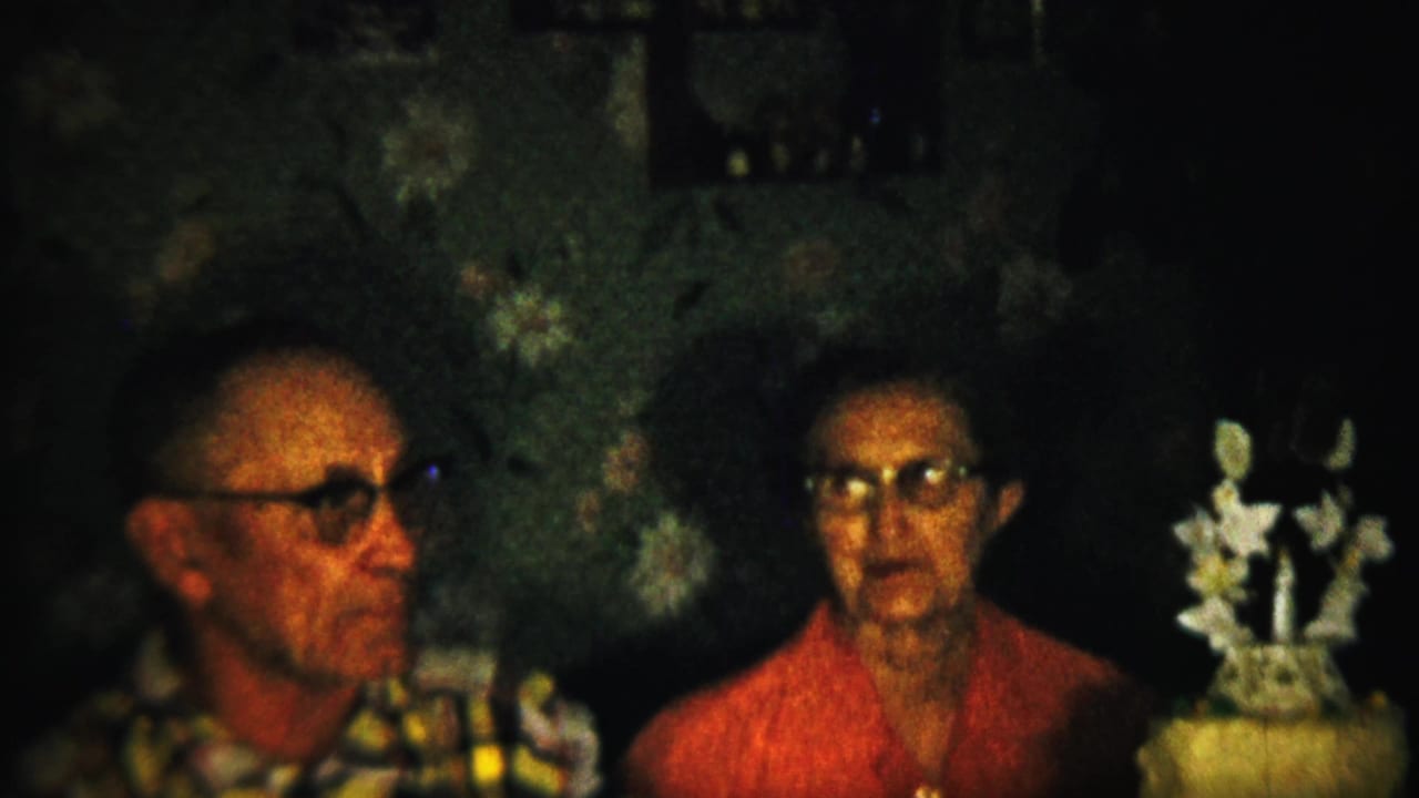 The elderly couple remains seated in a Saint Francis, Kansas interior, with the man turned slightly toward the woman and the decorated cake visible at the right edge.