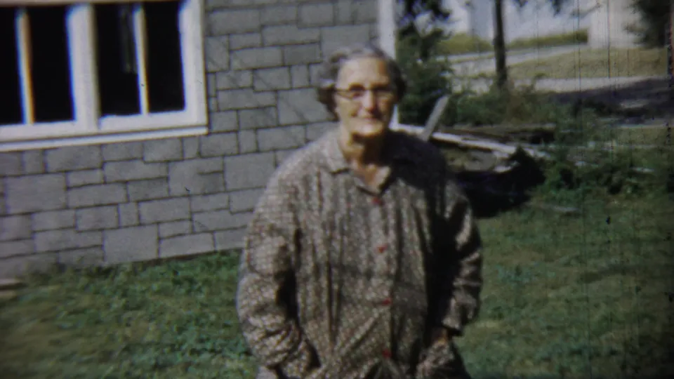 The 1959 home-movie frame shows the woman close to camera on a lawn beside the Chadron house exterior.