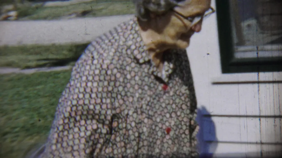 Near the end of the shot, the woman passes close to the house exterior and window while walking out of the yard frame.