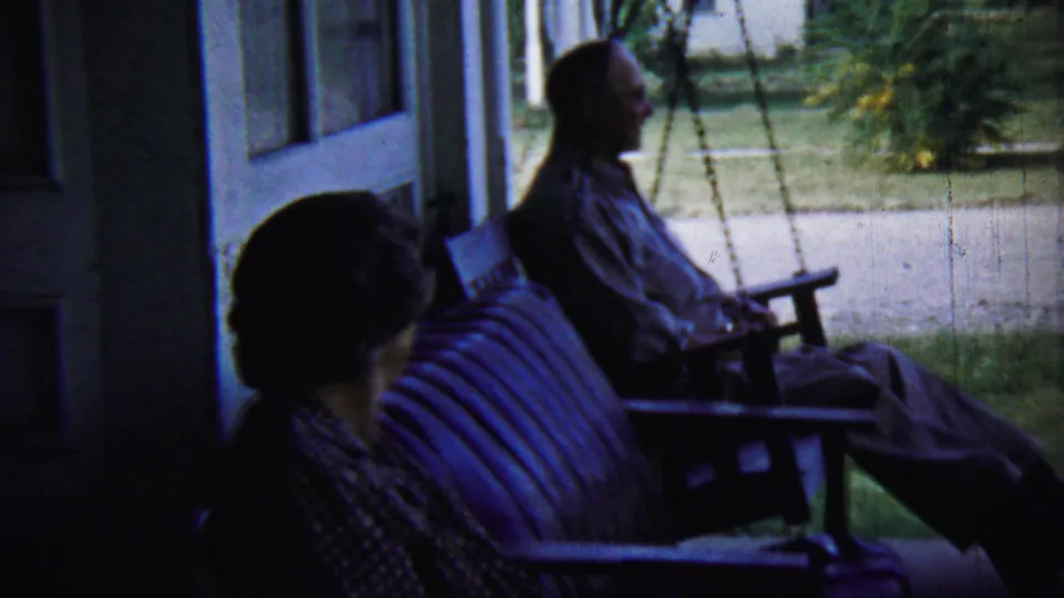 A shaded porch scene shows an older man seated on a swing and a woman seated nearby, with lawn and trees beyond.