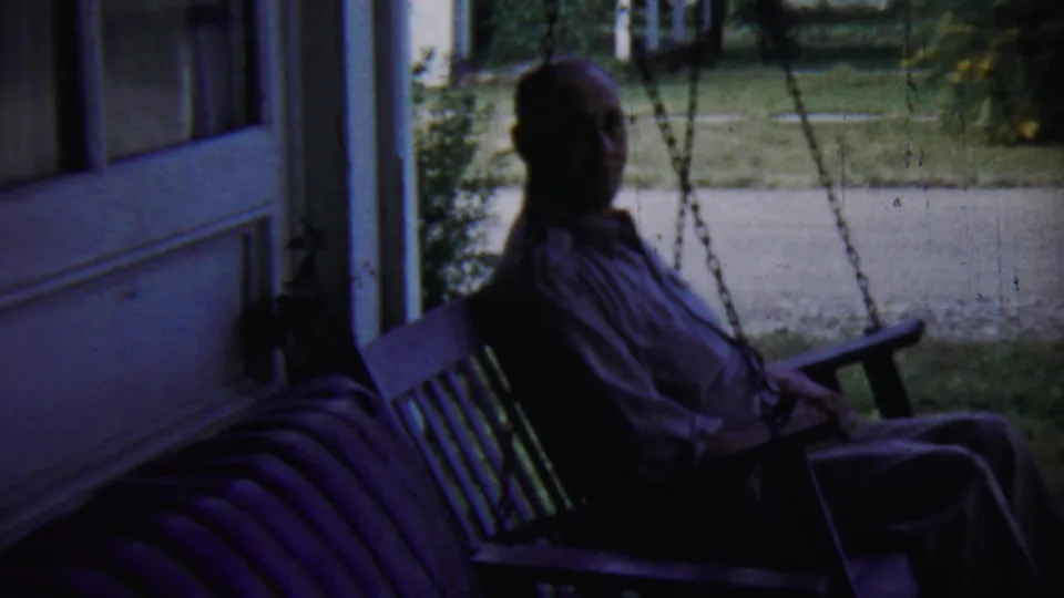 A closer 1959 home-movie view shows an older man seated on a porch swing, with a bench, open doors, lawn, and walkway visible.