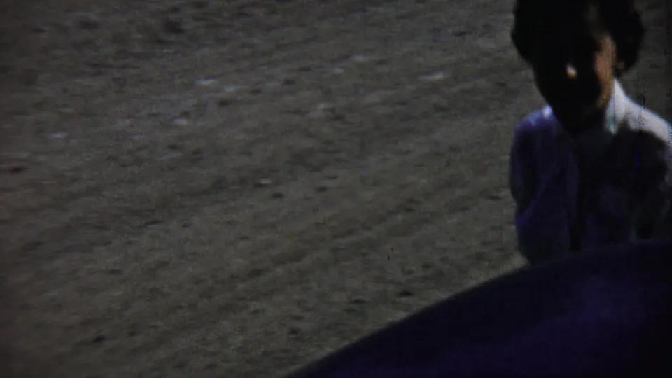 A dark, soft-focused frame shows an adult near the edge of a blue car on the gravel surface in Chadron, Nebraska.