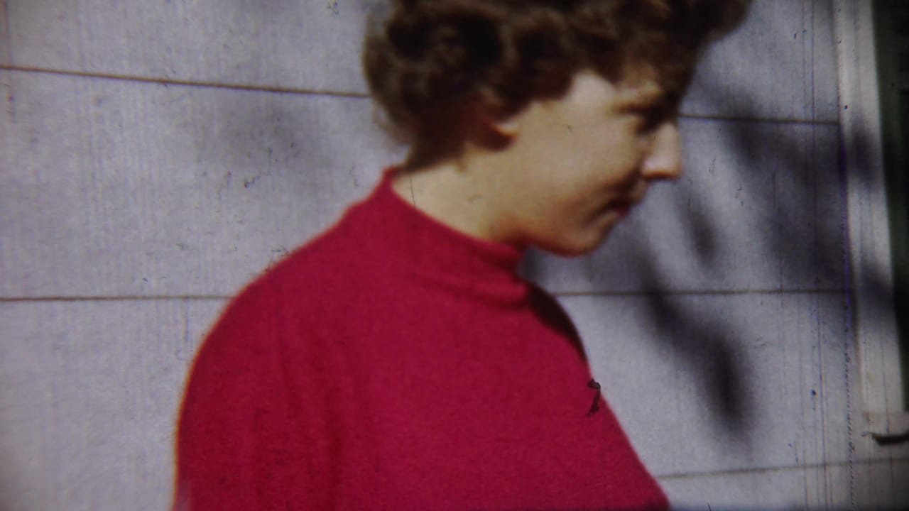 Young woman in a red turtleneck seen in profile beside a pale wall.
