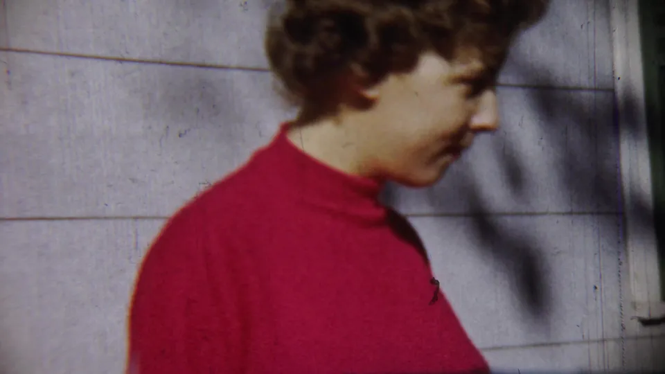 Young woman in a red turtleneck stands in profile near a pale wall in Chadron, Nebraska 1959 home-movie footage.