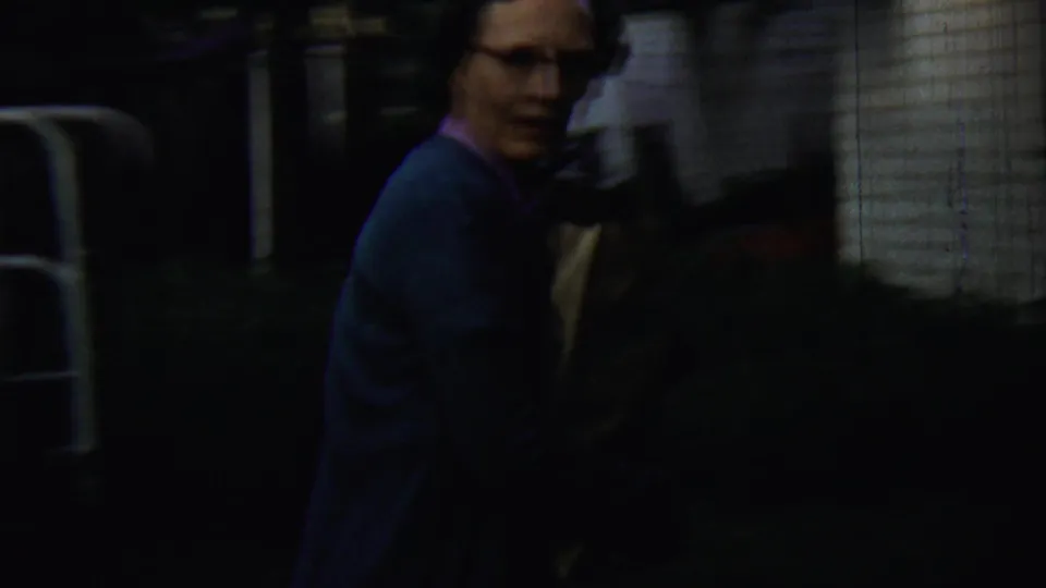 In Chadron, Nebraska home-movie footage from 1959, a woman in a blue cardigan is seen near a white-sided house at dusk.