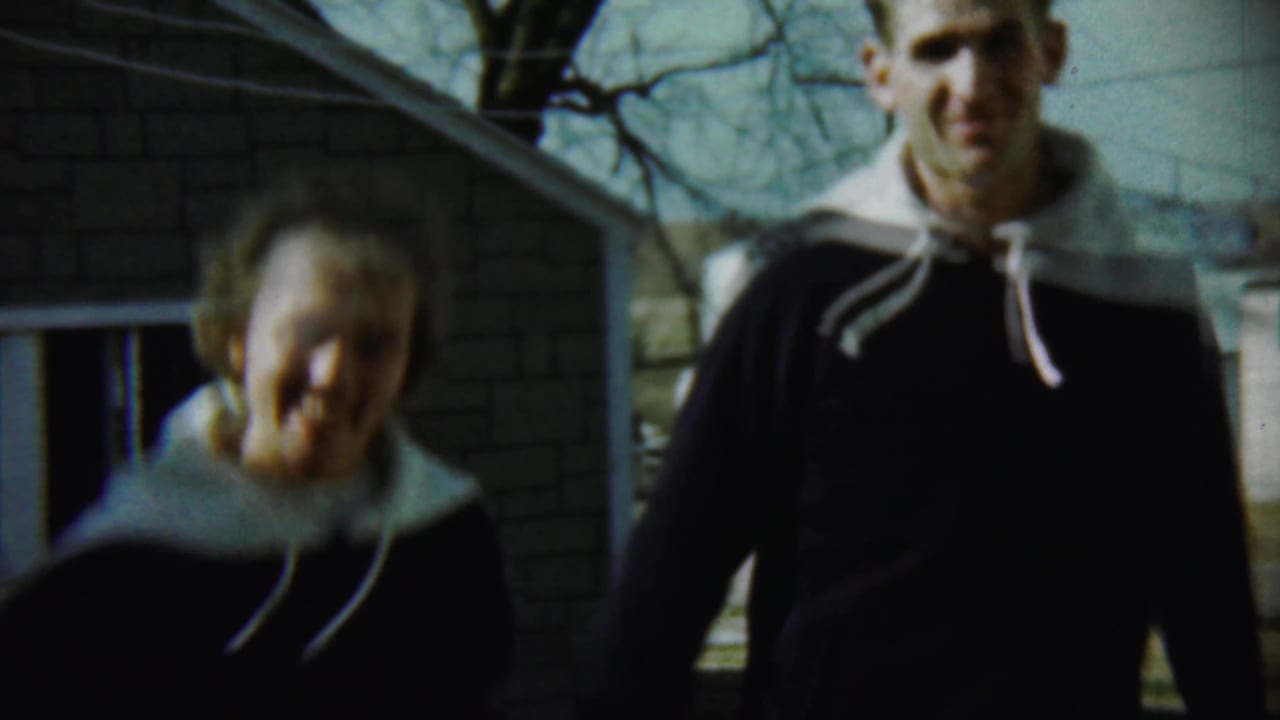 Young woman and young man in dark hooded sweaters near a brick house.