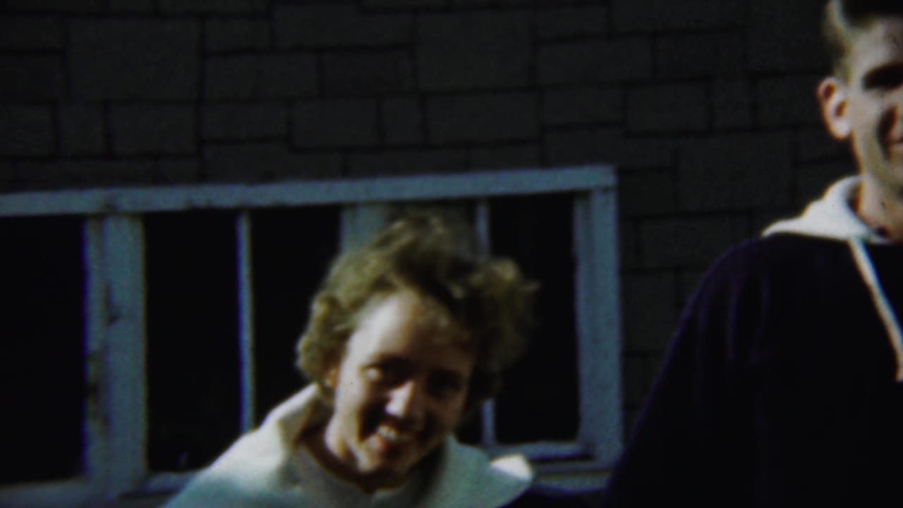 Young man and young woman smile near windows on a brick house.