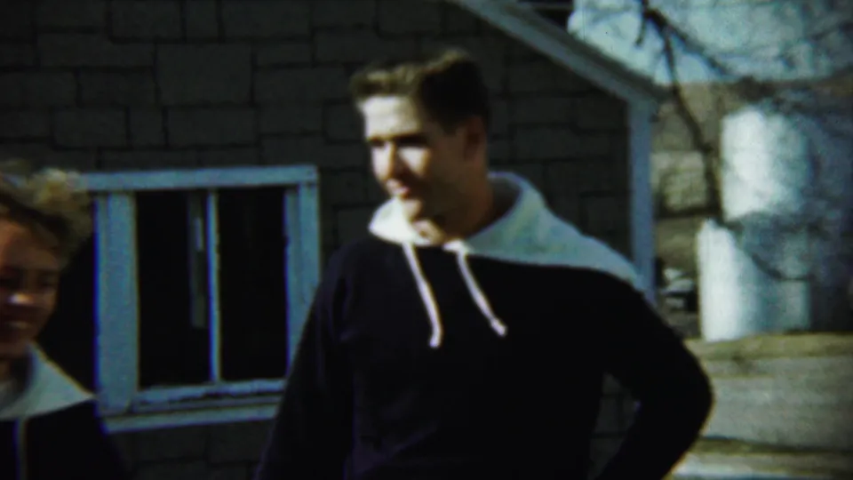 The man turns slightly away outside the Chadron house while the curly-haired woman is cropped at the left edge of the frame.
