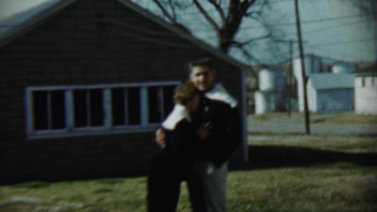 Young couple embracing on a lawn in front of a brick house.