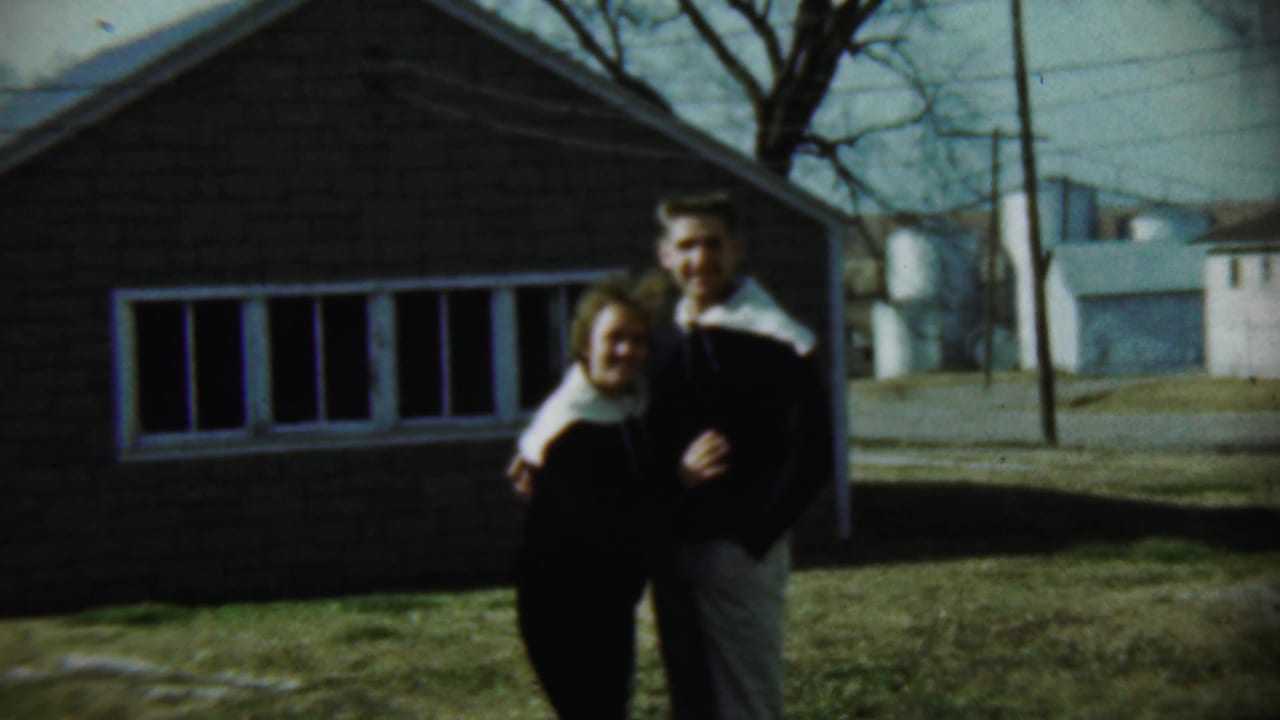 Couple facing the camera while holding each other outside a house.