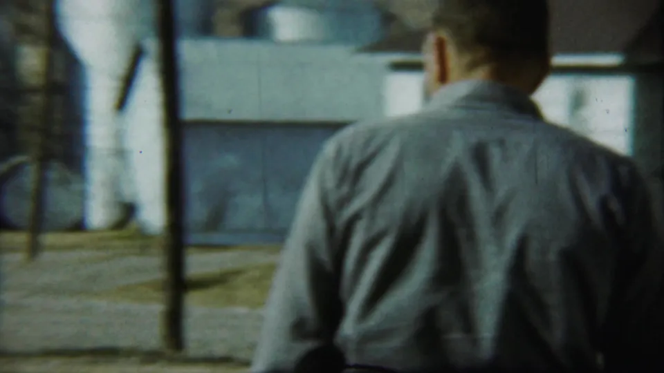 In 1959 Chadron, Nebraska footage, a man seen from behind approaches or frames a smiling couple standing outside a gray shingled house.