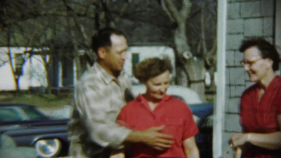 In Chadron, Nebraska in 1959, adults pose outside a shingled house as a man in plaid embraces a woman in a red top.
