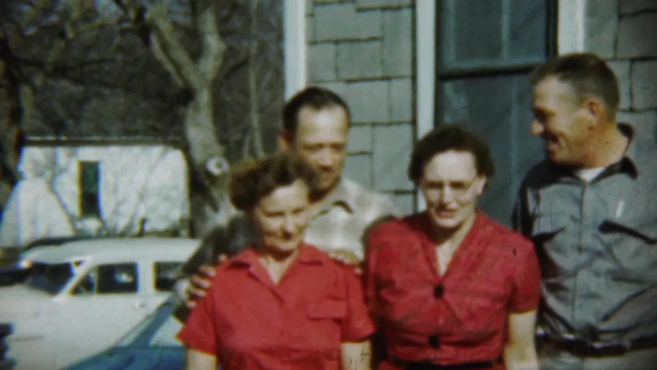 Four adults in 1959 Chadron stand together outside a shingled house, with a light-colored parked car and bare trees behind them.