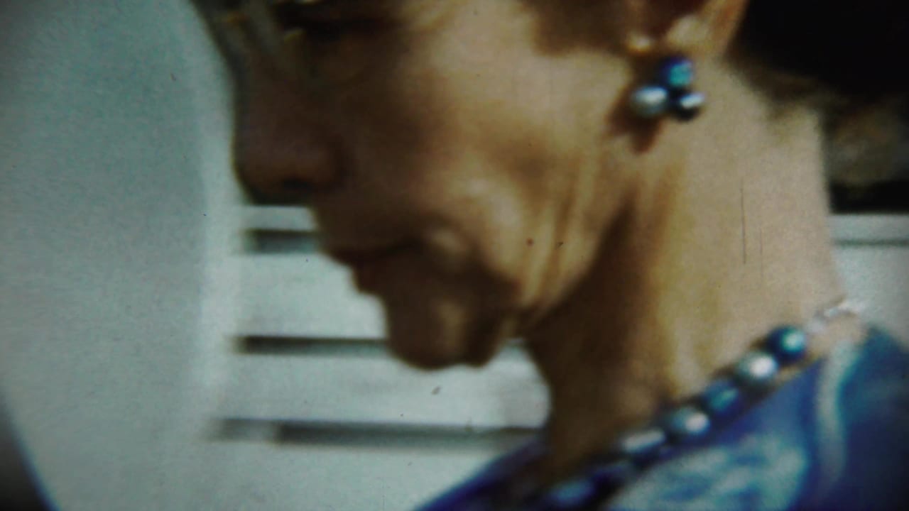Soft close-up of a woman's profile with blue jewelry and a blurred exterior wall behind her.
