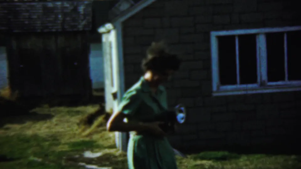 In the 1959 Chadron home-movie footage, a woman in a green dress walks past the building while holding a camera with a flash attachment.