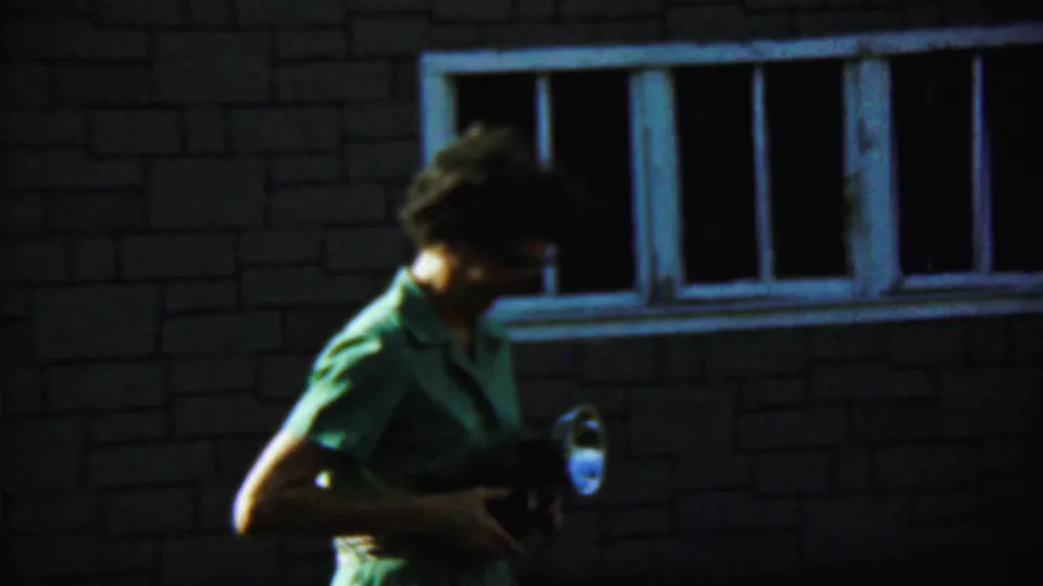 A woman in a green dress holds a vintage flash camera in front of a white-framed window and dark masonry wall in Chadron, Nebraska.