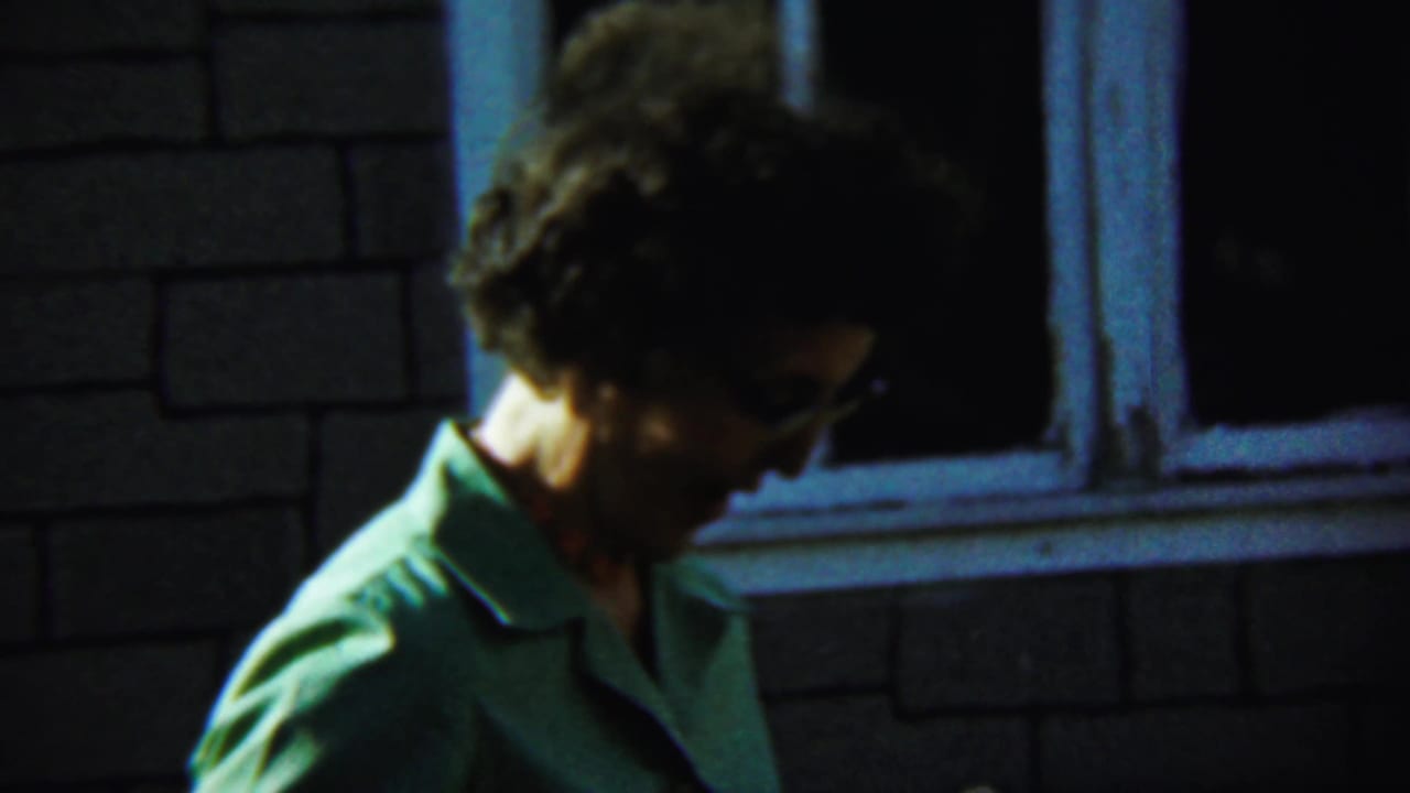 Woman in profile stands near a window with her face partly shadowed.