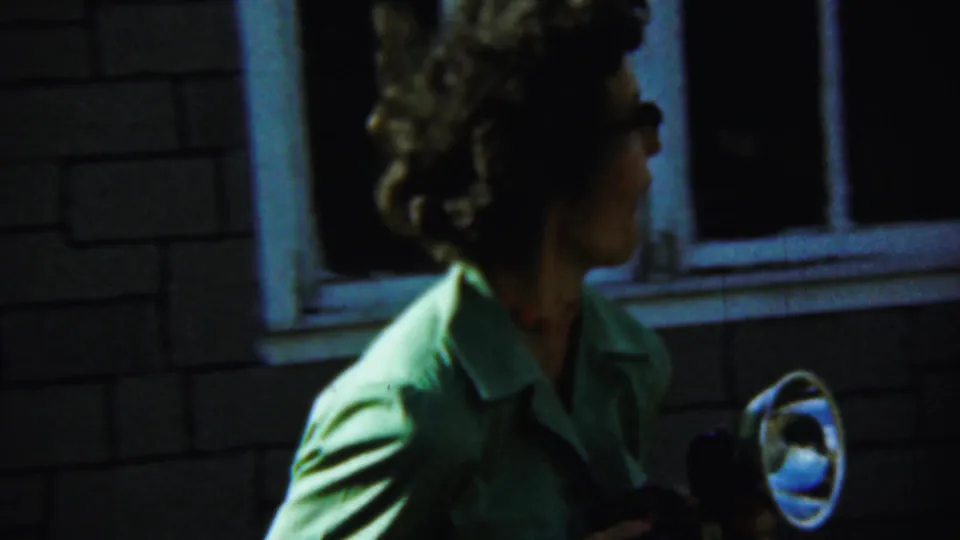 The woman faces sideways with the flashlight visible near her hand, framed against the dark window and brick wall in Chadron.