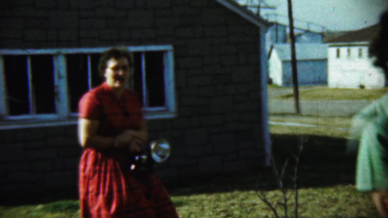 Woman in a red dress holding a camera near a house and yard.